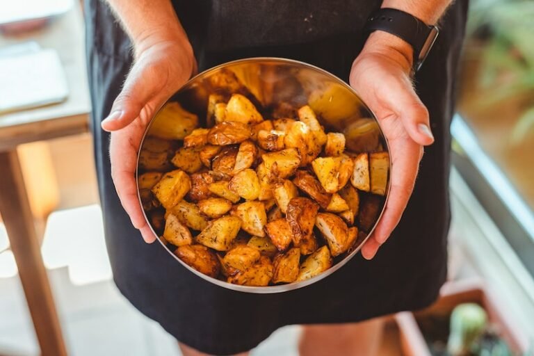 From above of crop anonymous male chef in apron standing with bowl of potato wedges